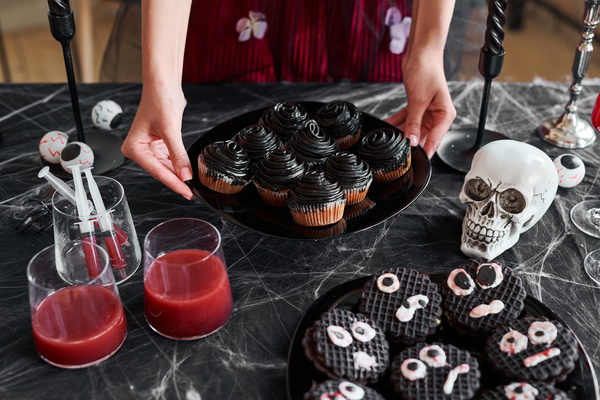 Girl Puts Plate with Cupcakes on Table Decorated for Halloween
